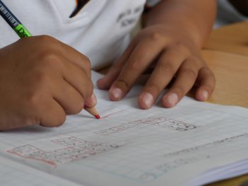 Young student writes numbers on grid paper, using pencil
